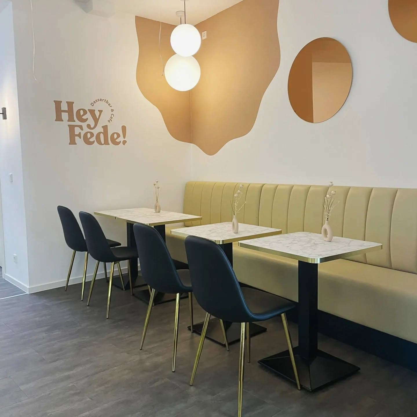 Sitzbereich mit Hey Fede! Logo an der Wand, gelbe Polsterbank und Marmortische in Wetzlar